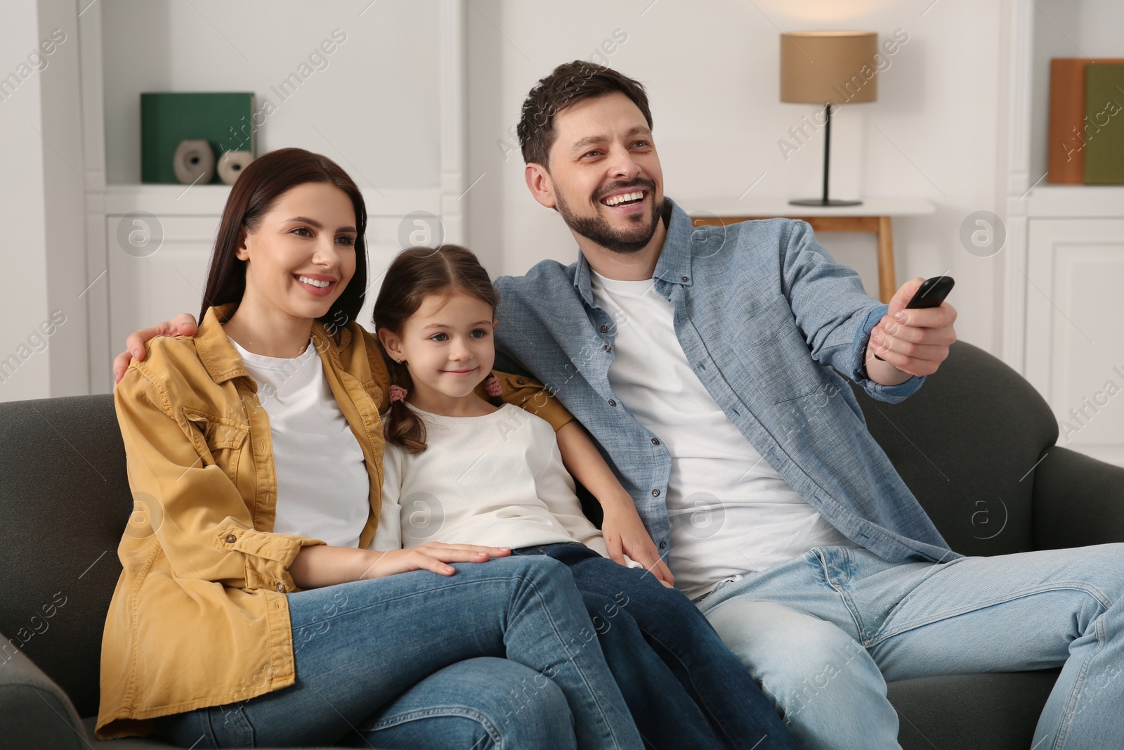 Photo of Happy family watching movie at home. Father changing TV channels with remote control