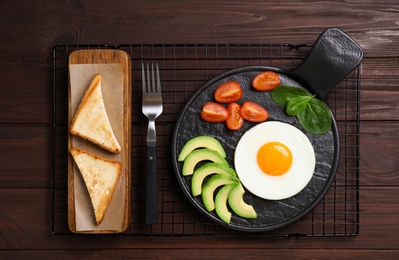 Photo of Tasty breakfast with fried egg, toasts and avocado served on wooden table, flat lay
