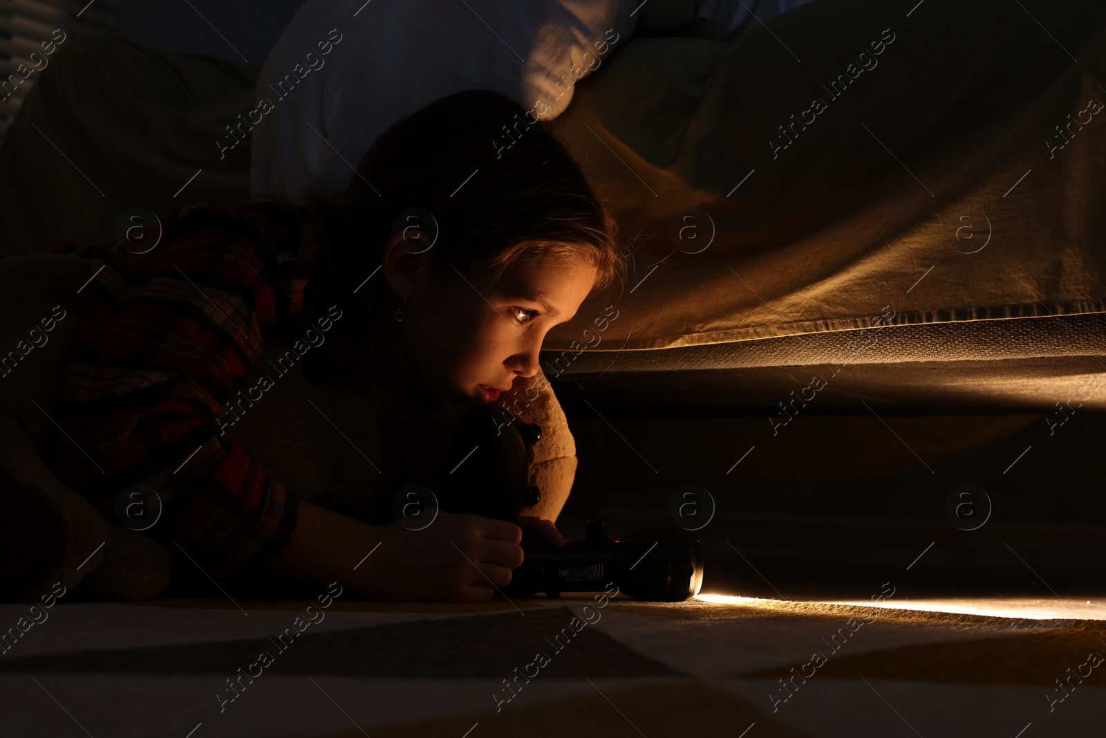 Photo of Little girl with flashlight looking for monster under bed at night