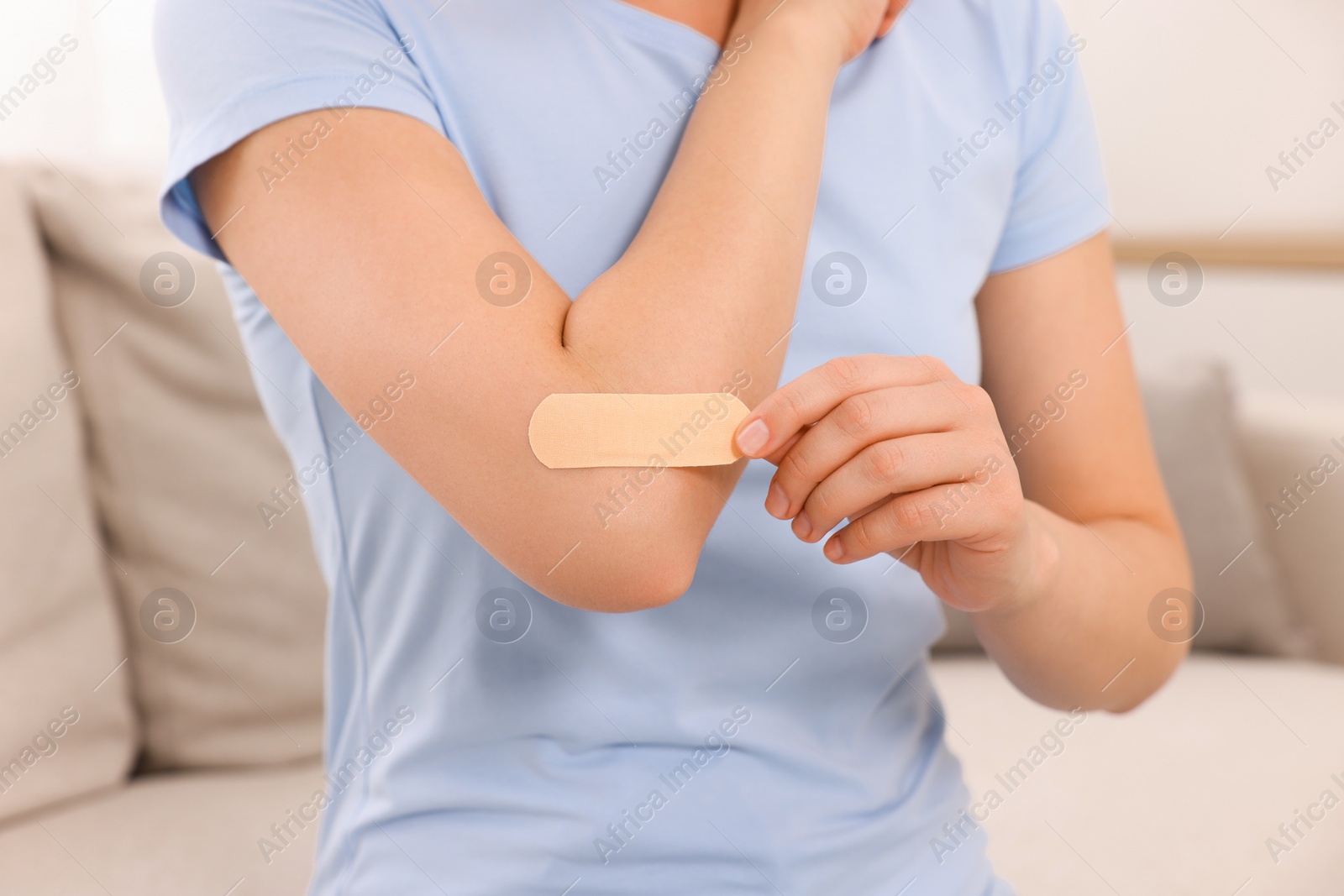 Photo of Woman putting sticking plaster onto elbow indoors, closeup