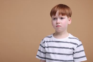 Portrait of sad little boy on beige background, space for text