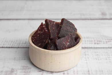Delicious beef jerky in bowl on white wooden table