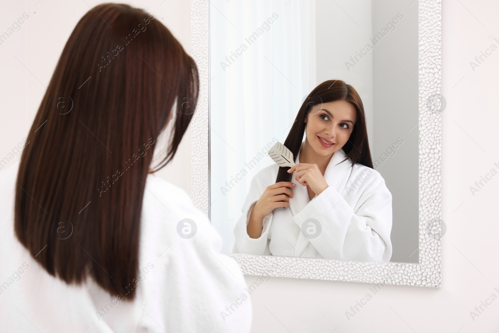 Photo of Beautiful woman brushing her hair near mirror indoors