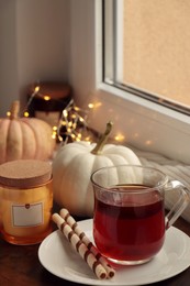 Photo of Cup of hot drink, cookies, candle and pumpkins on window sill indoors