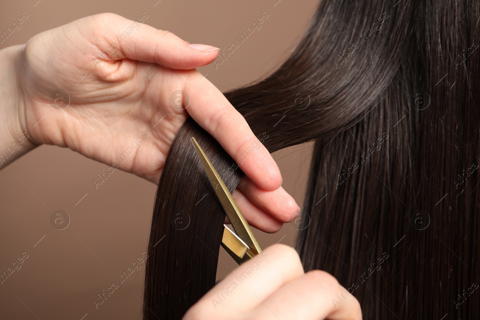 Photo of Hairdresser cutting client's hair with scissors on light brown background, closeup