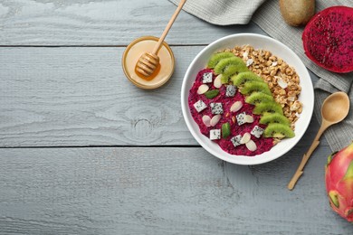 Photo of Bowl of granola with pitahaya, kiwi and almonds served on grey wooden table, flat lay. Space for text