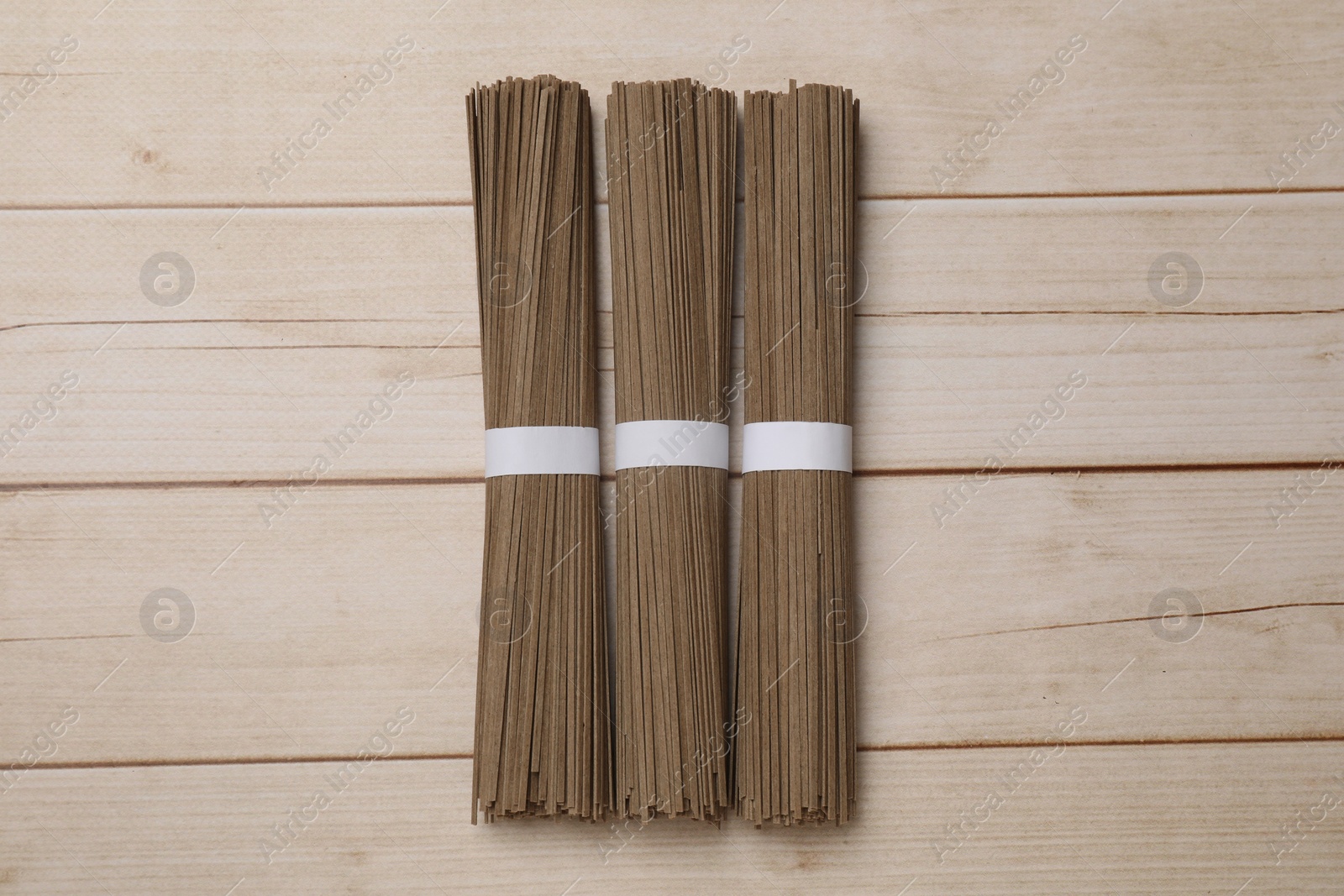 Photo of Uncooked buckwheat noodles (soba) on light wooden table, flat lay