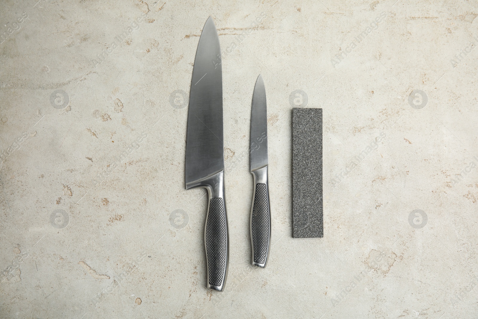 Photo of Sharpening stone and knives on grey table, flat lay