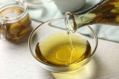 Pouring fresh olive oil into bowl on table