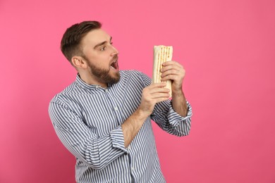 Emotional young man with delicious shawarma on pink background