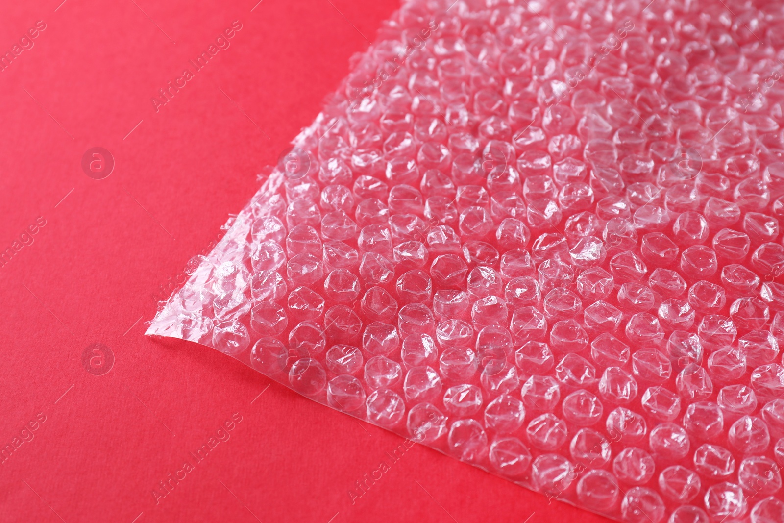 Photo of Transparent bubble wrap on red background, closeup