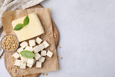 Photo of Delicious tofu cheese, basil and soybeans on light gray table, flat lay. Space for text