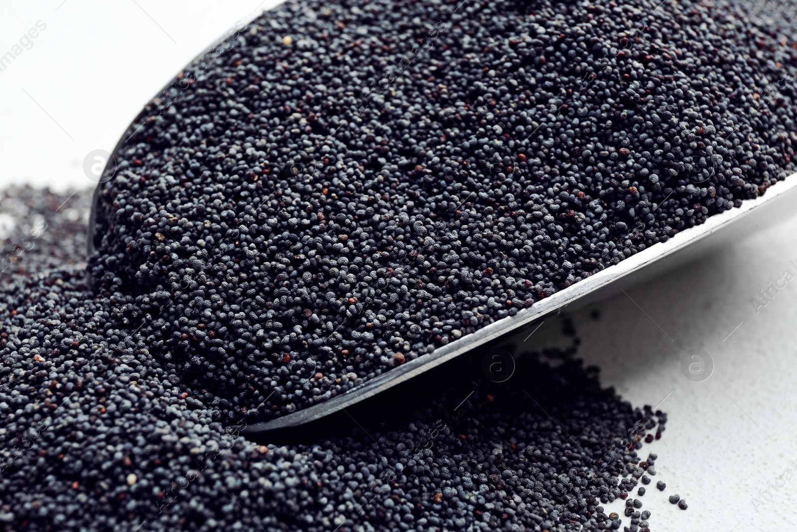 Photo of Poppy seeds in metal scoop on white table, closeup