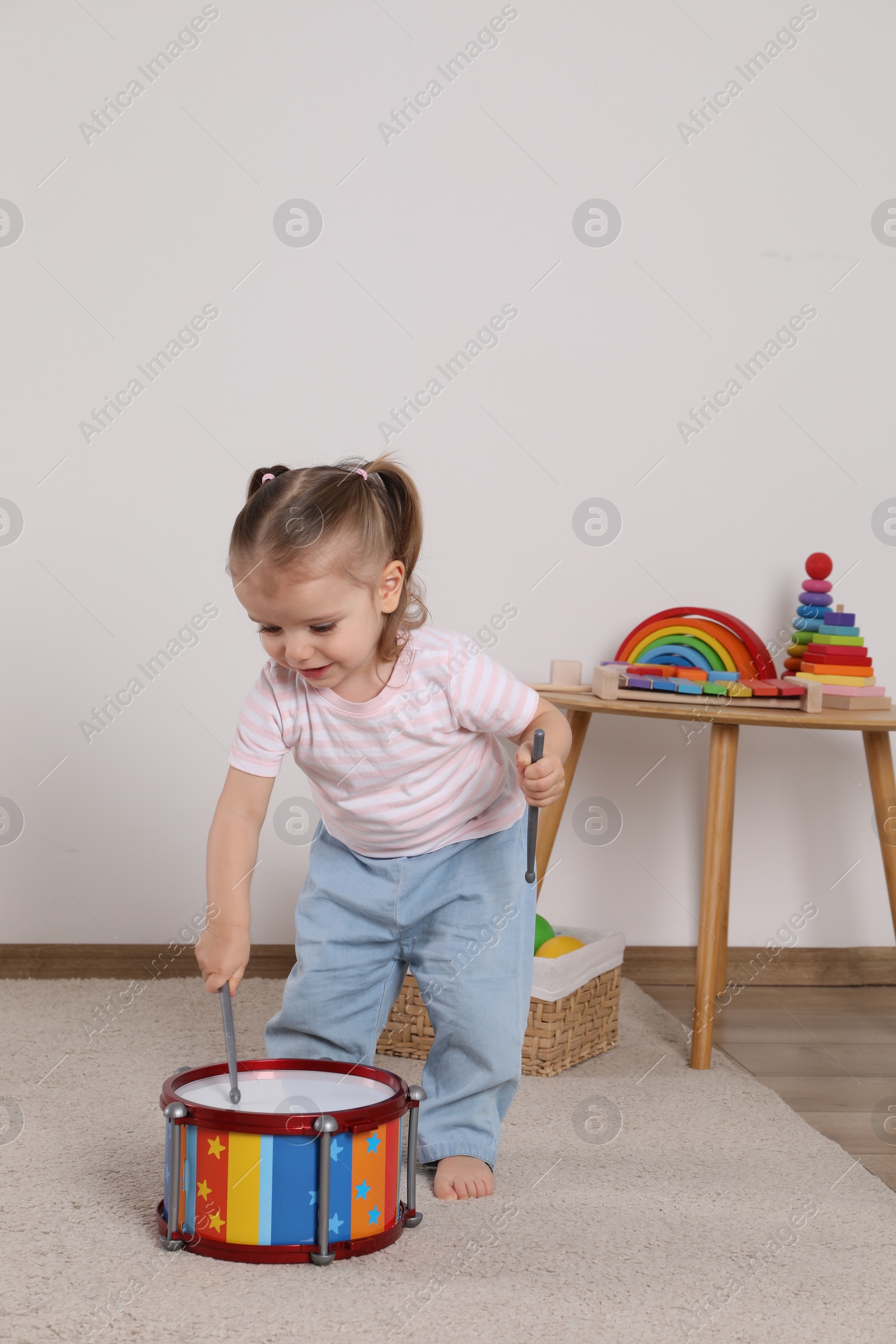 Photo of Cute little girl playing with drum and drumsticks at home