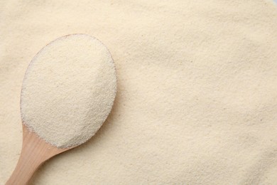 Photo of Uncooked organic semolina and wooden spoon, top view. Space for text