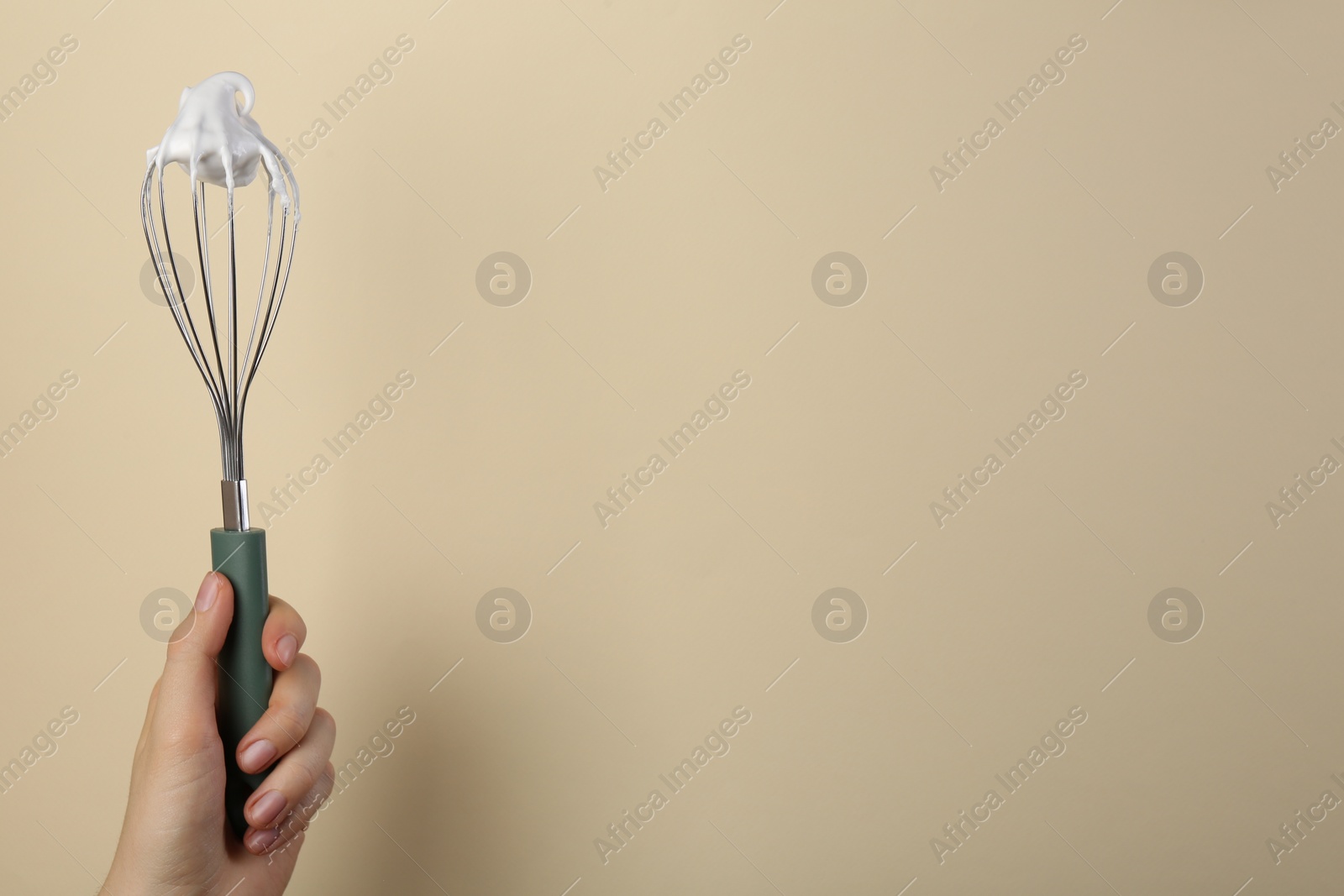Photo of Woman holding whisk with whipped cream on beige background, closeup. Space for text