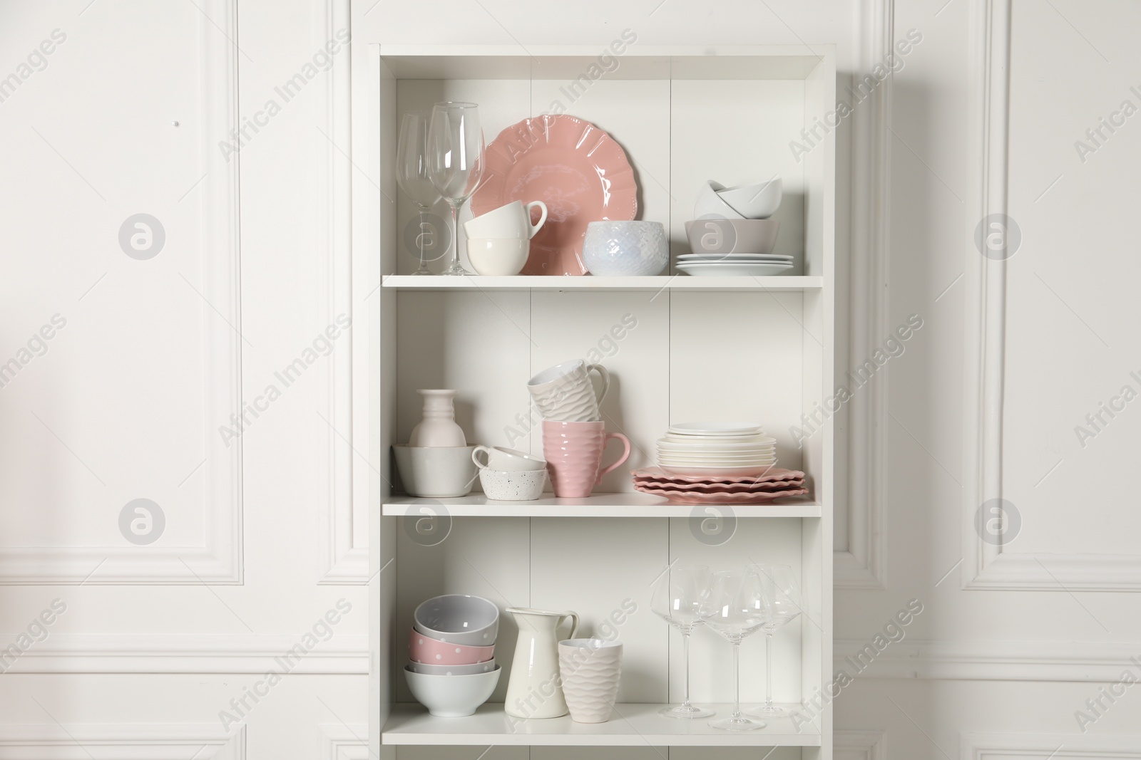 Photo of Different ceramic dishware and glasses on shelves in cabinet indoors