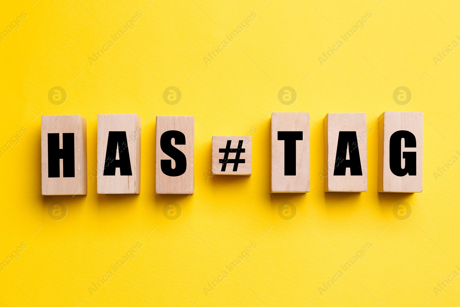 Photo of Wooden blocks with word Hashtag and symbol on yellow background, flat lay