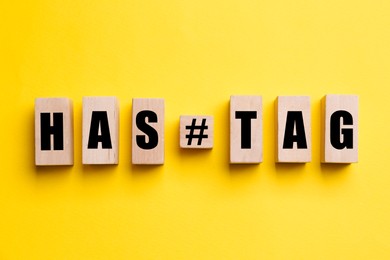 Photo of Wooden blocks with word Hashtag and symbol on yellow background, flat lay