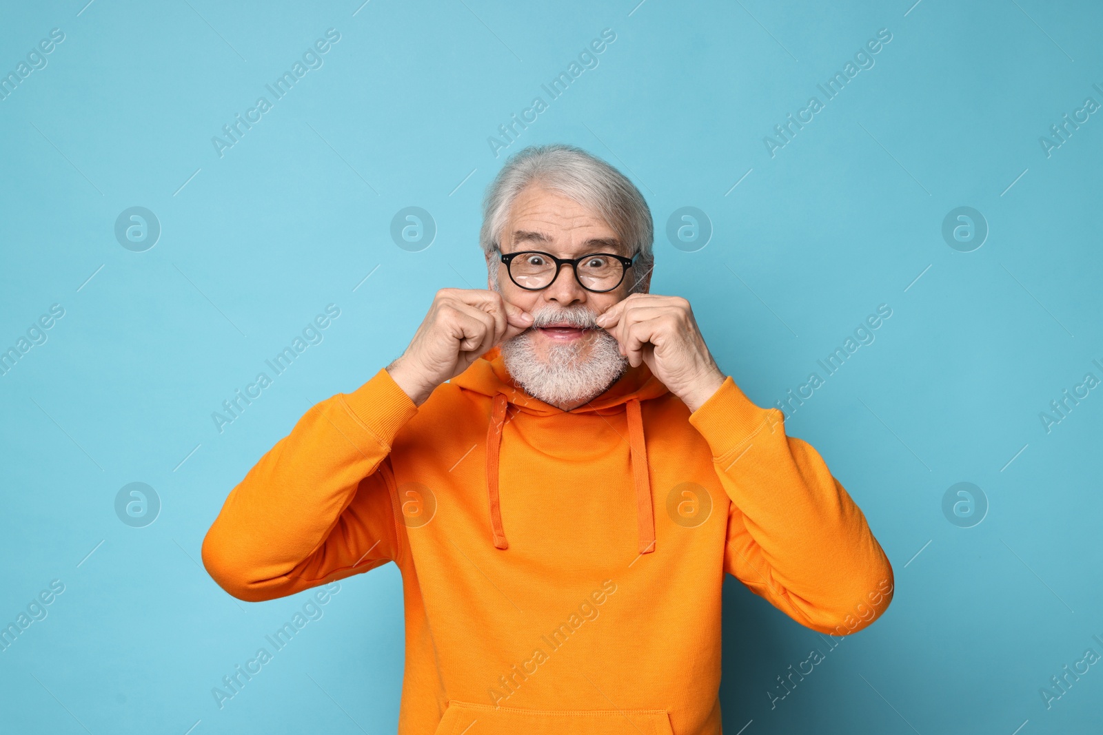 Photo of Senior man touching mustache on light blue background