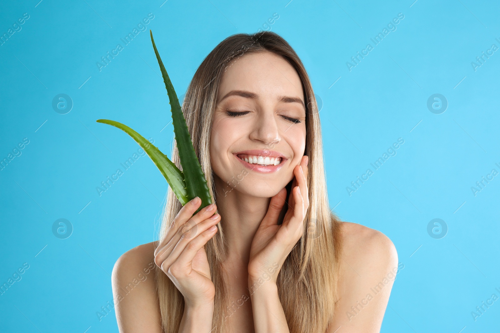 Photo of Happy young woman with aloe leaves on light blue background