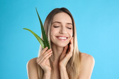 Photo of Happy young woman with aloe leaves on light blue background