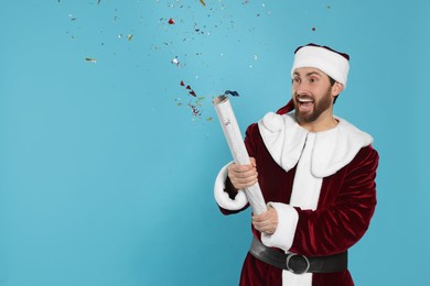 Photo of Emotional man in Santa Claus costume blowing up party popper on light blue background. Space for text