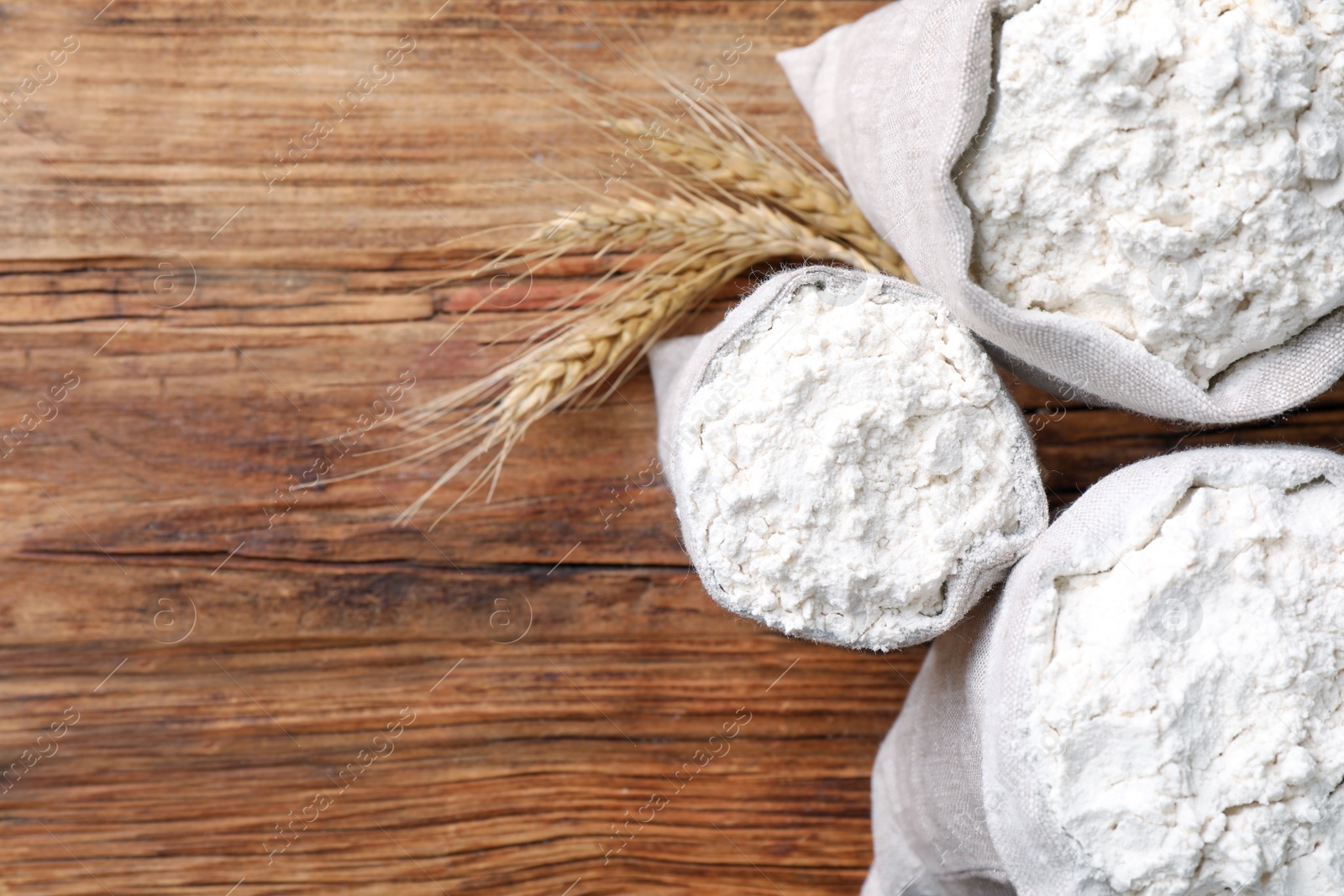 Photo of Sacks with flour and wheat spikes on wooden background, flat lay. Space for text