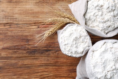 Photo of Sacks with flour and wheat spikes on wooden background, flat lay. Space for text