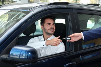 Photo of Young salesman giving car key to client in dealership