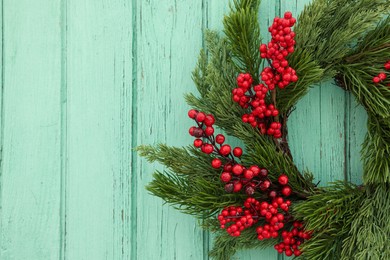 Beautiful Christmas wreath with red berries hanging on turquoise wooden wall, closeup. Space for text