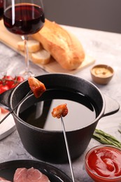 Photo of Fondue pot, forks with fried meat pieces and other products on grey textured table