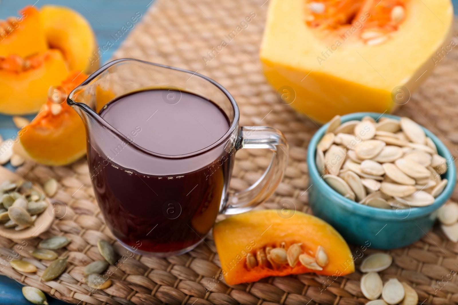 Photo of Fresh pumpkin seed oil in glass pitcher on blue wooden table