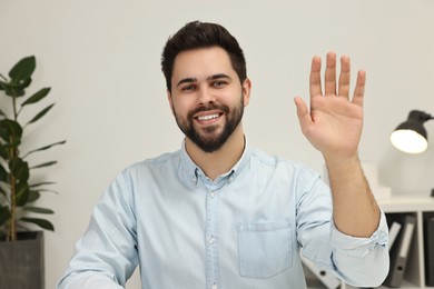 Photo of Happy young man waving hello during video chat indoors, view from web camera