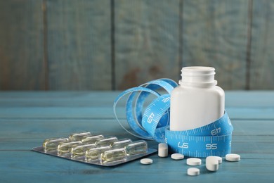 Photo of Weight loss pills and measuring tape on light blue wooden table. Space for text