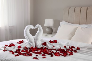 Beautiful swans made of towels and red rose petals on bed in room