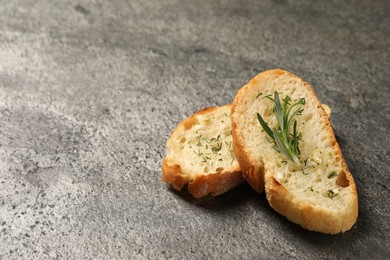 Tasty baguette with garlic, rosemary and dill on grey textured table, closeup. Space for text
