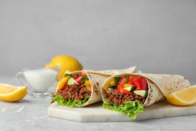 Board with delicious meat tortilla wraps on light table against grey background. Space for text