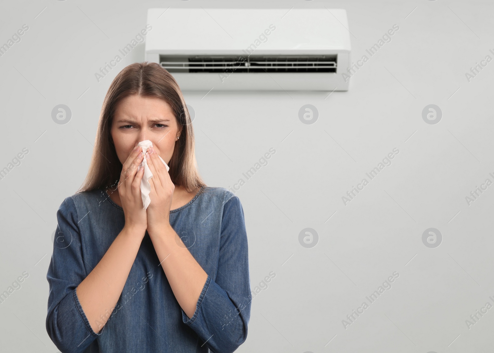 Image of Woman suffering from cold in room with air conditioner on white wall, space for text