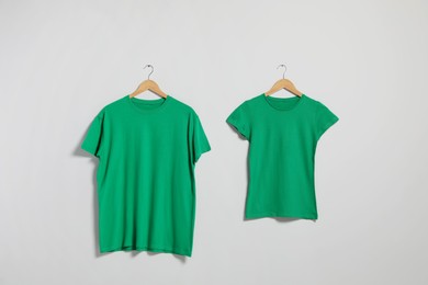 Photo of Hangers with different t-shirts on light wall. Mockup for design