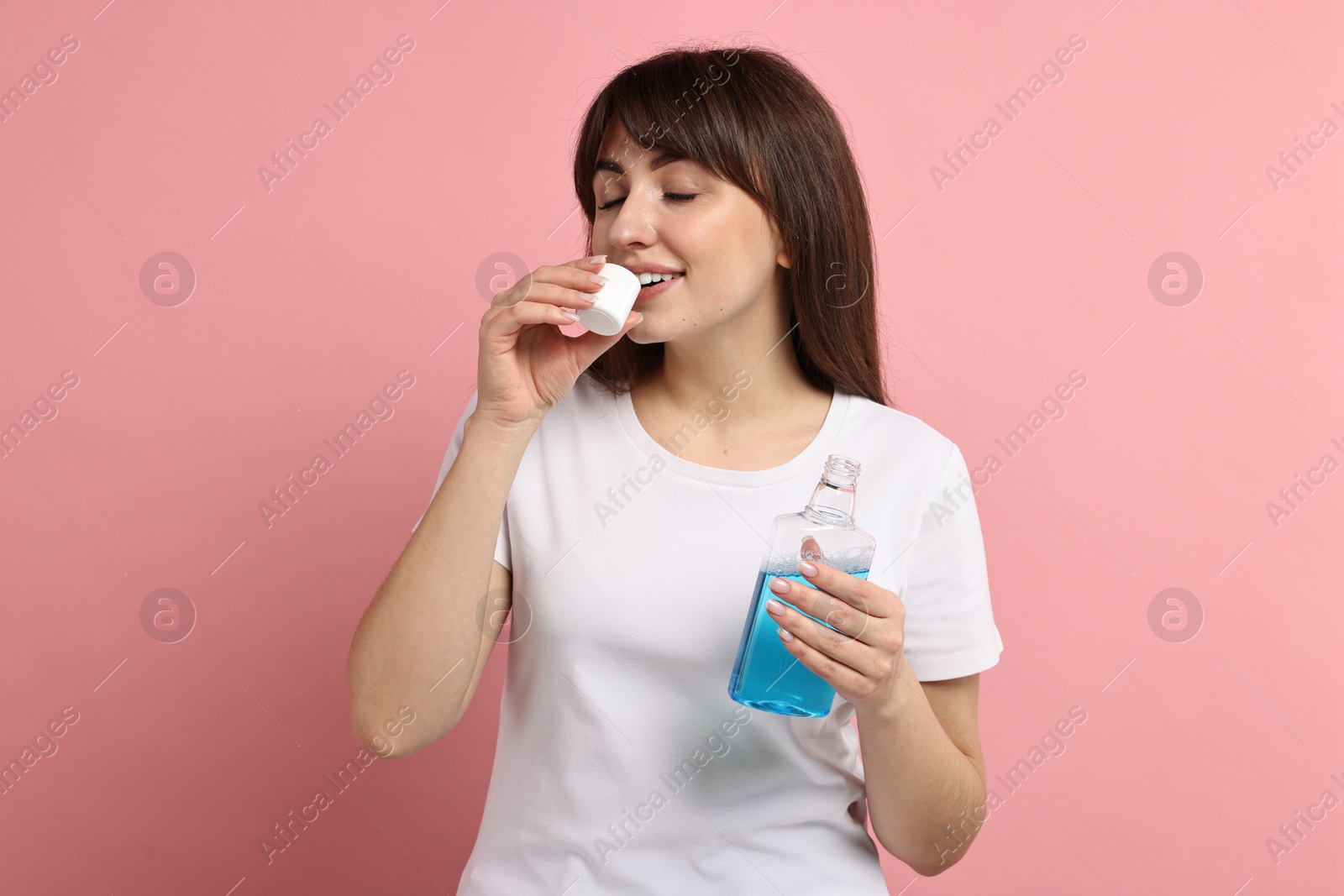 Photo of Young woman using mouthwash on pink background