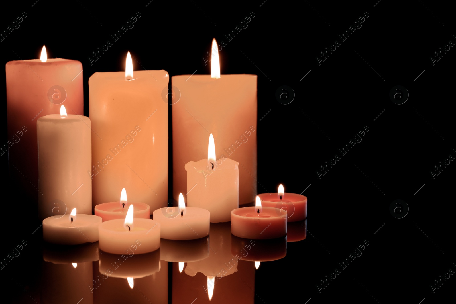 Photo of Different wax candles burning on black background