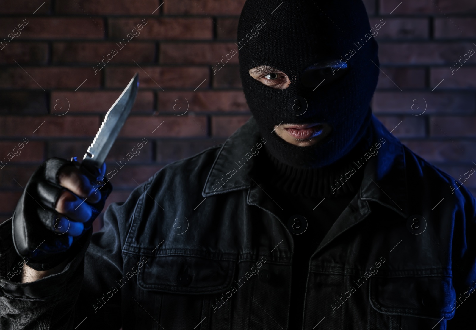 Photo of Man in mask with knife near brick wall. Dangerous criminal