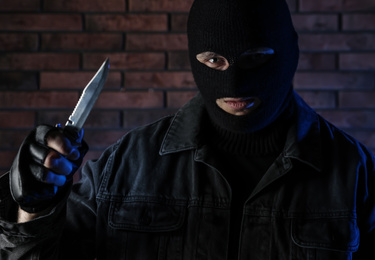 Man in mask with knife near brick wall. Dangerous criminal