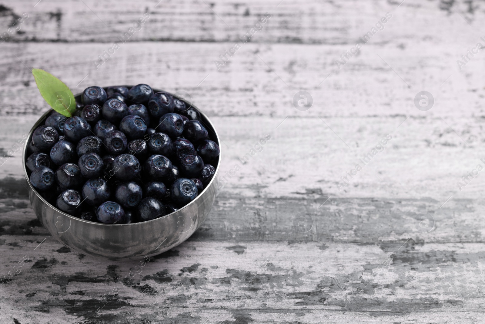 Photo of Ripe bilberries and leaf in bowl on wooden rustic table. Space for text