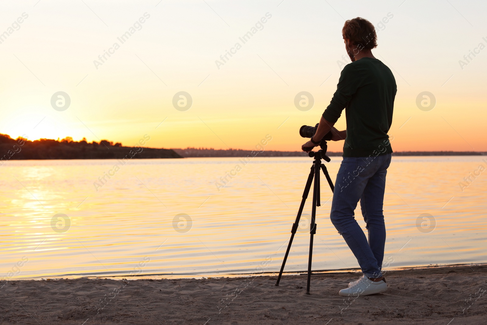 Photo of Young male photographer standing with professional camera on riverside