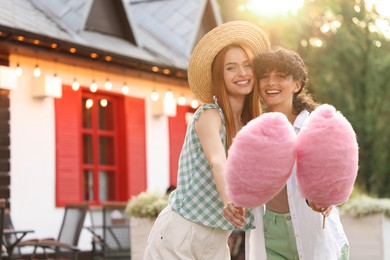 Photo of Happy friends with pink cotton candies outdoors. Space for text