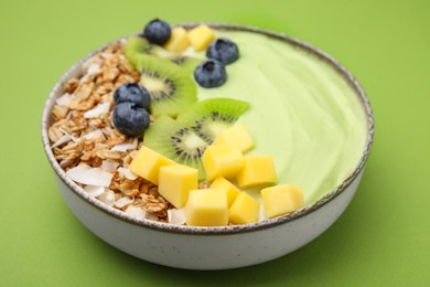 Photo of Tasty matcha smoothie bowl served with fresh fruits and oatmeal on green background, closeup. Healthy breakfast