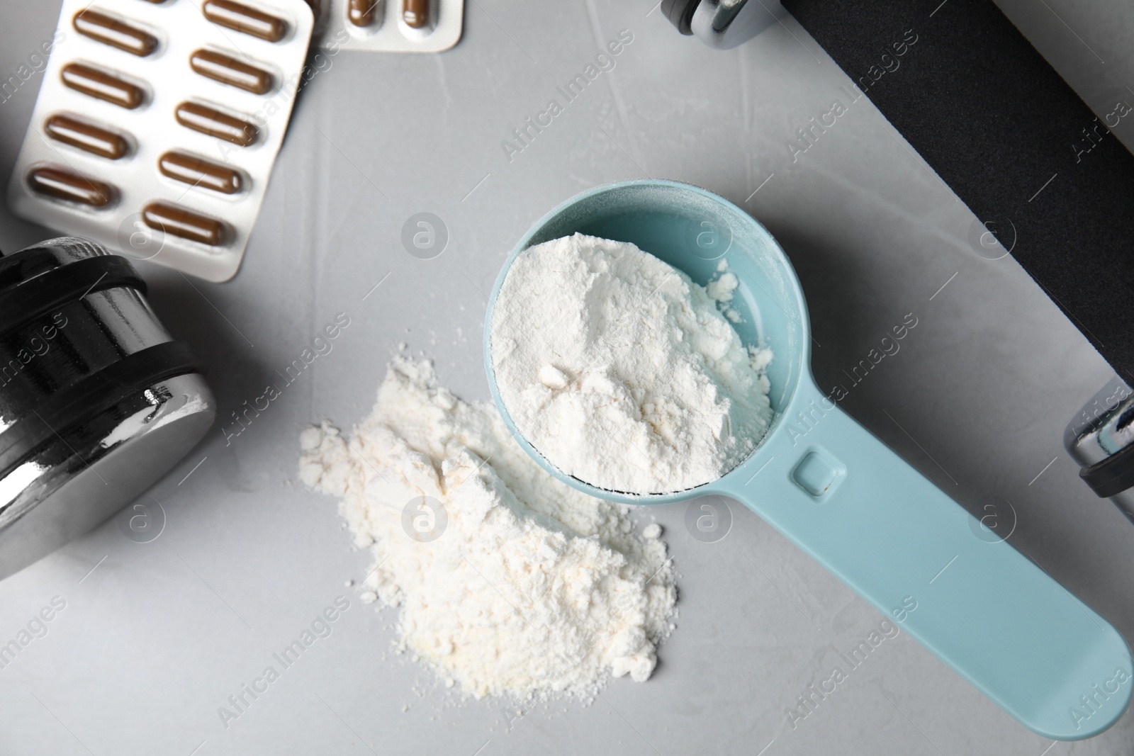 Photo of Measuring scoop of amino acids powder, pills and dumbbells on light grey table, flat lay