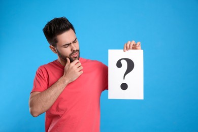 Photo of Emotional young man with question mark sign on light blue background